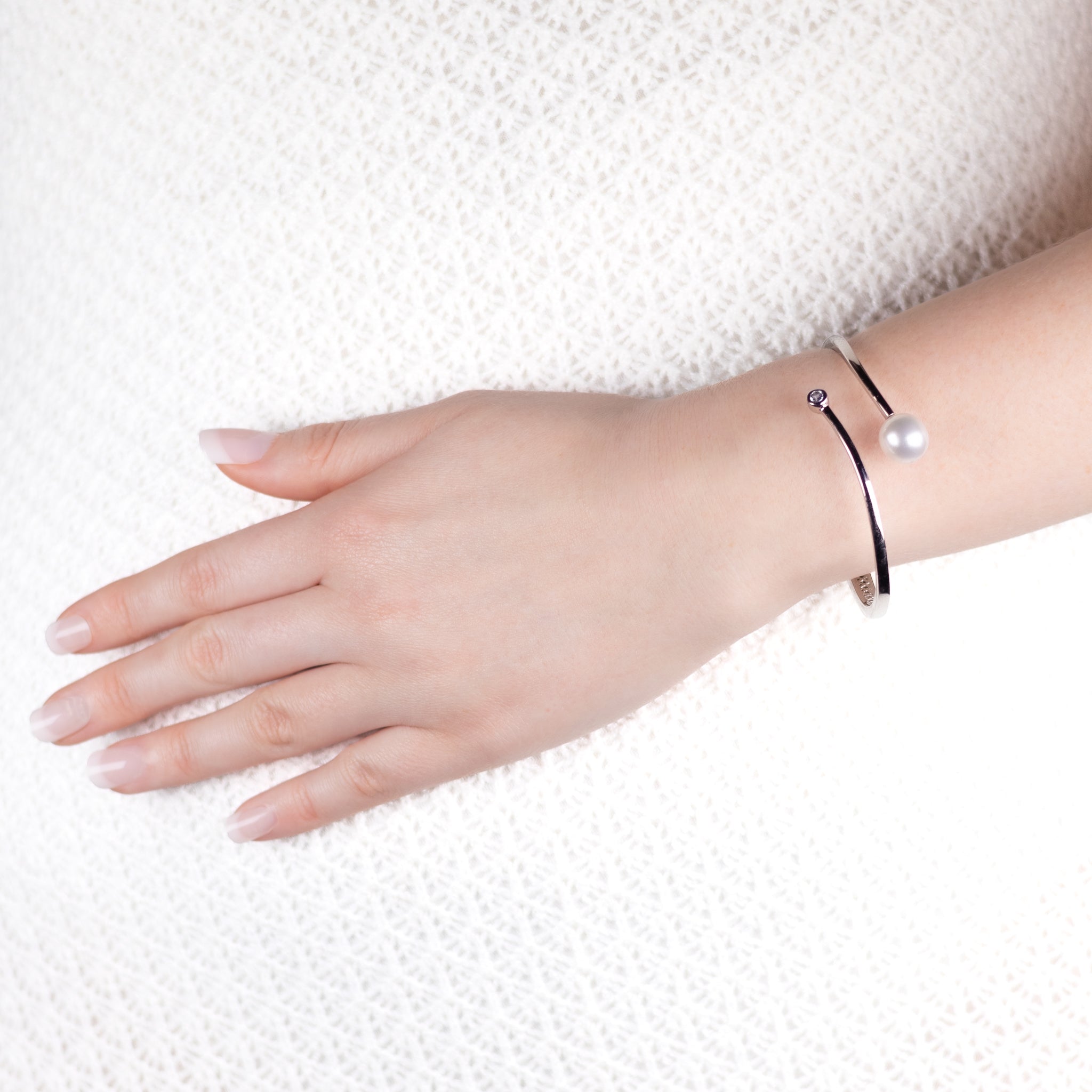 Hand wearing a black bracelet with a pearl on a white background