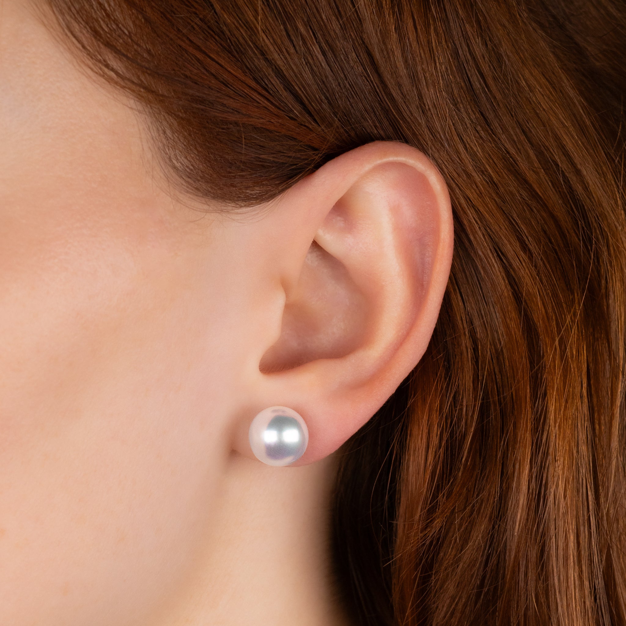 Close-up of an ear wearing a pearl stud earring with brown hair.