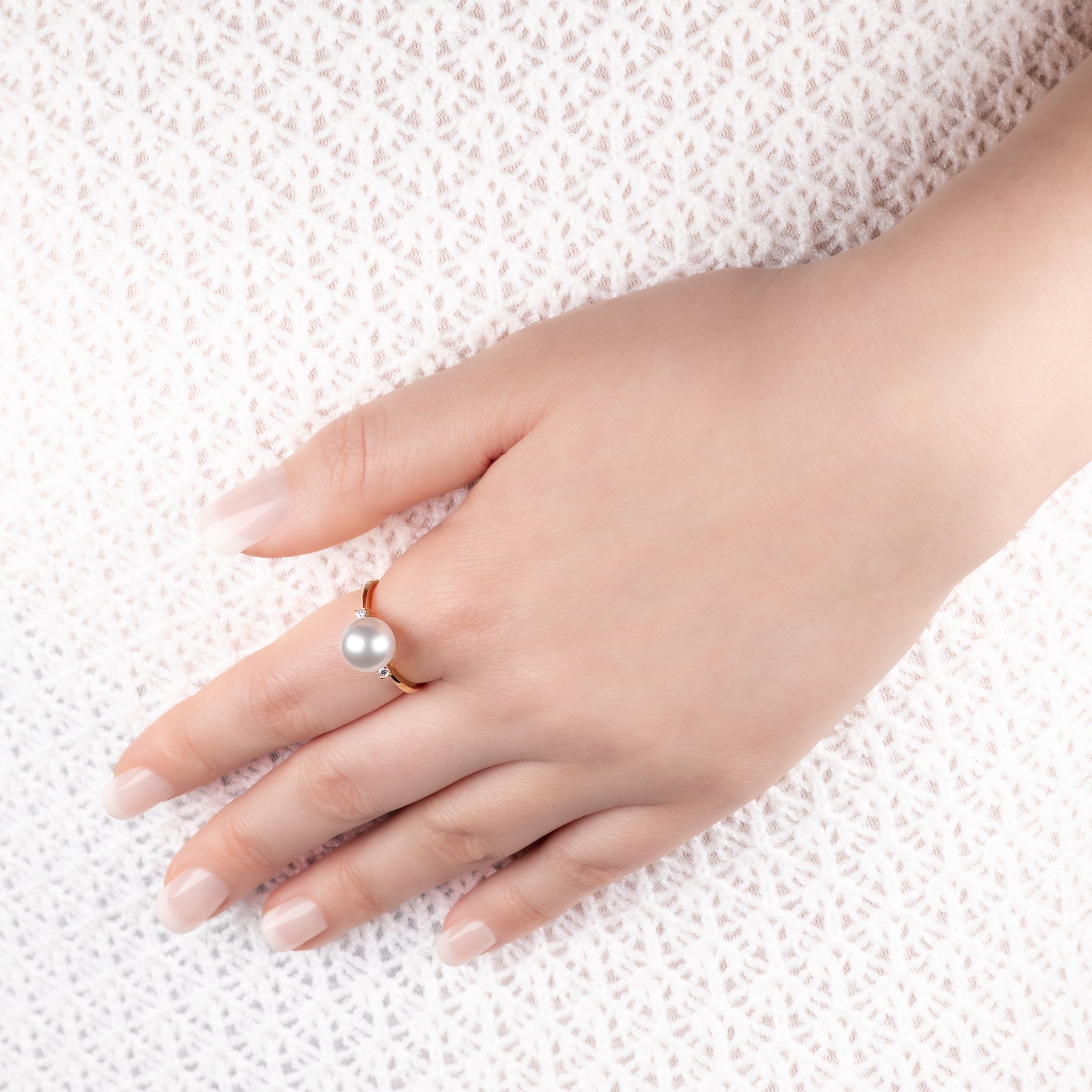 Hand wearing 18K Yellow Gold Australian South Sea 9-10 mm Cultured Pearl and Diamond Ring on a textured white background