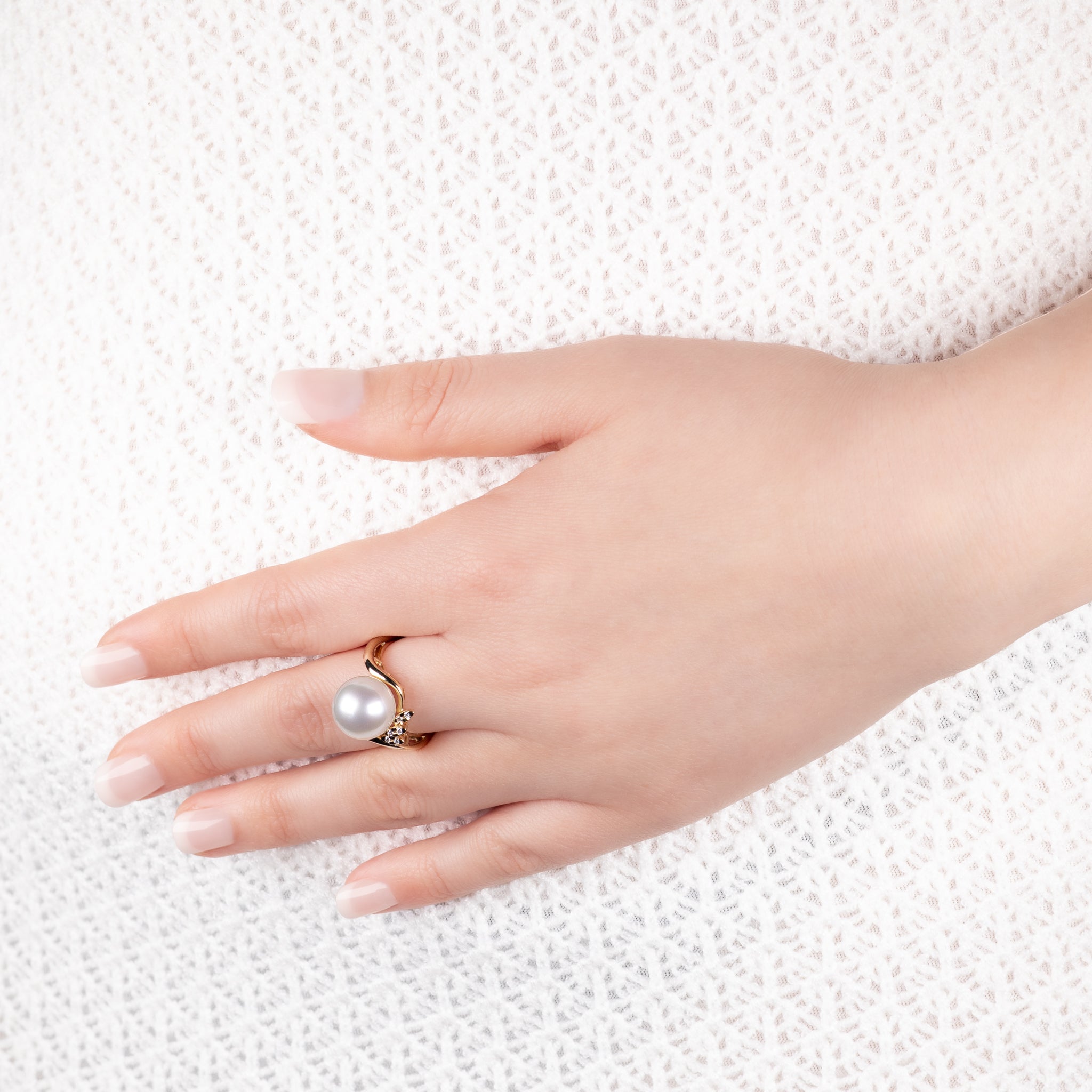 Hand wearing a pearl ring on a textured white background