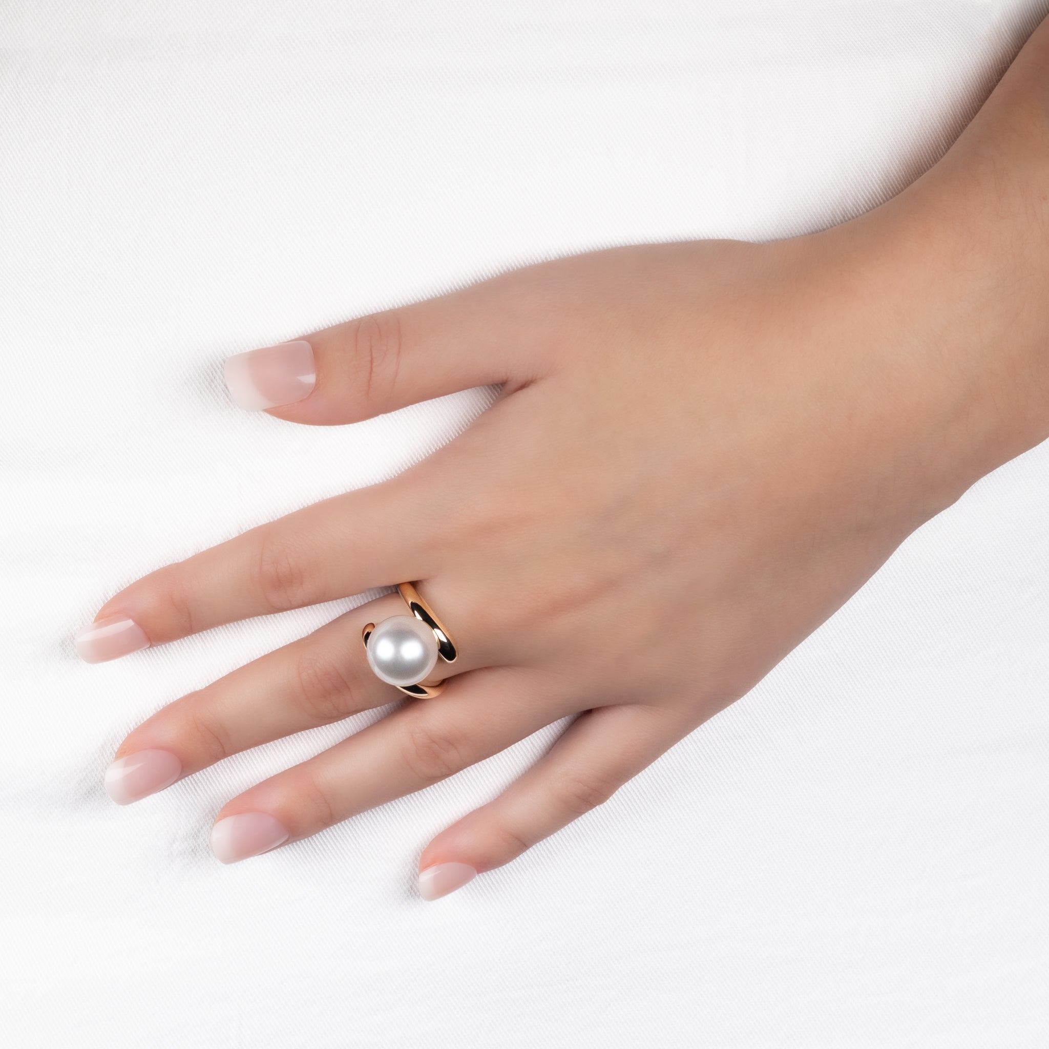 Hand wearing a pearl ring on a white background