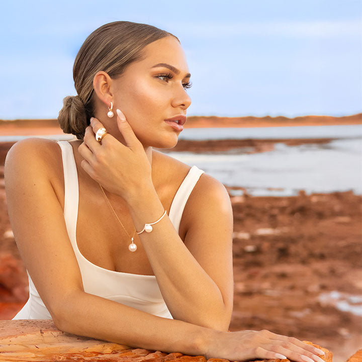 Woman wearing pearl drop gold pearl earrings from Australia, looking out over Broome landscape