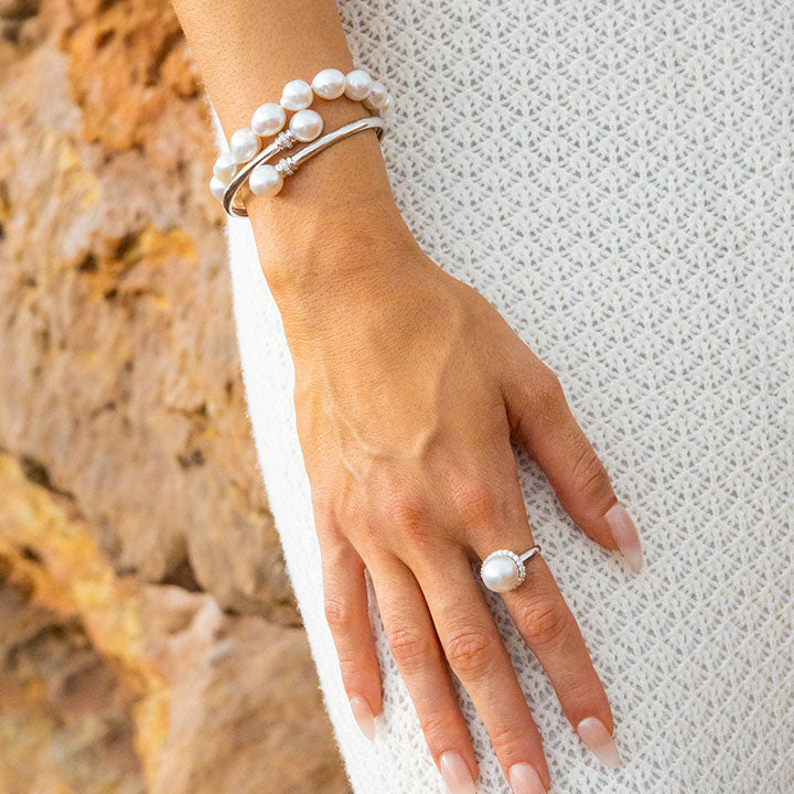 Hand wearing a cultured pearl bracelet and pearl ring against a textured white fabric background