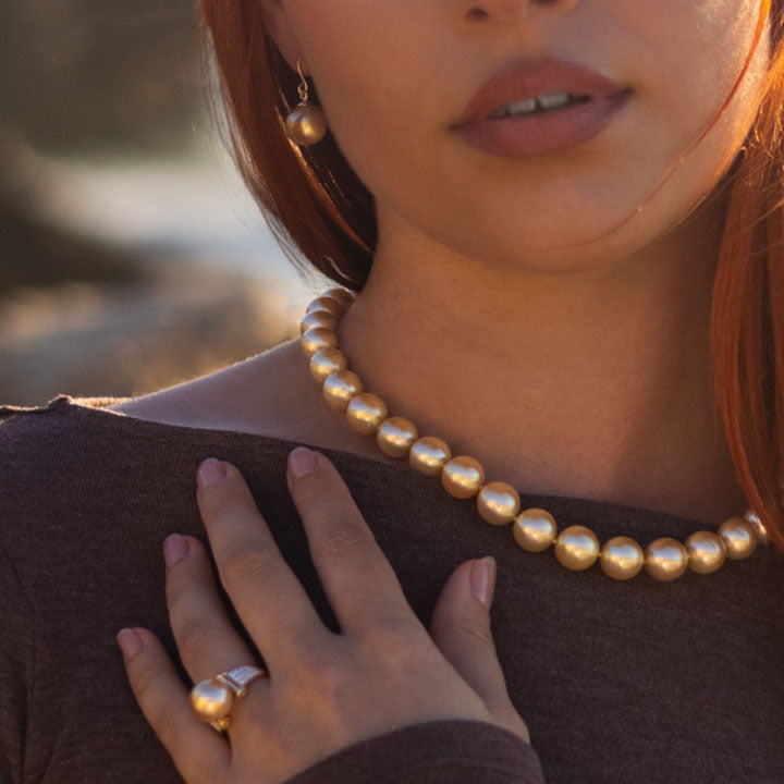 Close-up of a woman wearing a golden pearl necklace and gold pearl ring with a blurred background