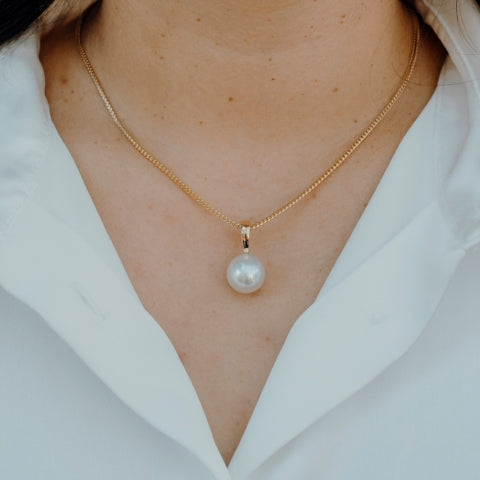 18k Yellow Gold Australian south sea pendant on a gold foxtail chain around a woman's neck wearing a white shirt
