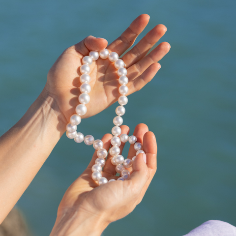Person holding a pearl necklace with a blurred natural background