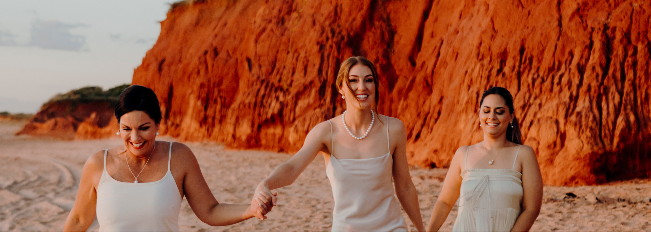Three women standing on a beach with red Broome cliffs in the background wearing beautiful Australian South Sea Pearl Jewellery