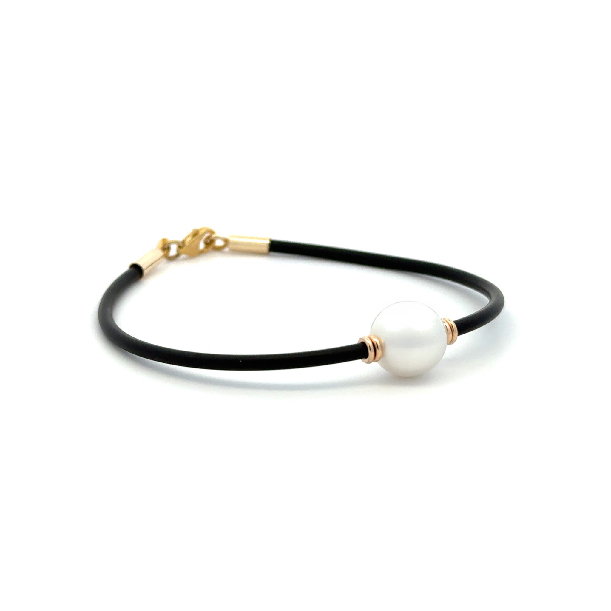 Side view of our black Neoprene Pearl Bracelet with 9k yellow gold clasp, with an Australian South Sea Peal cupped wither side by two yellow gold like beads on a white background