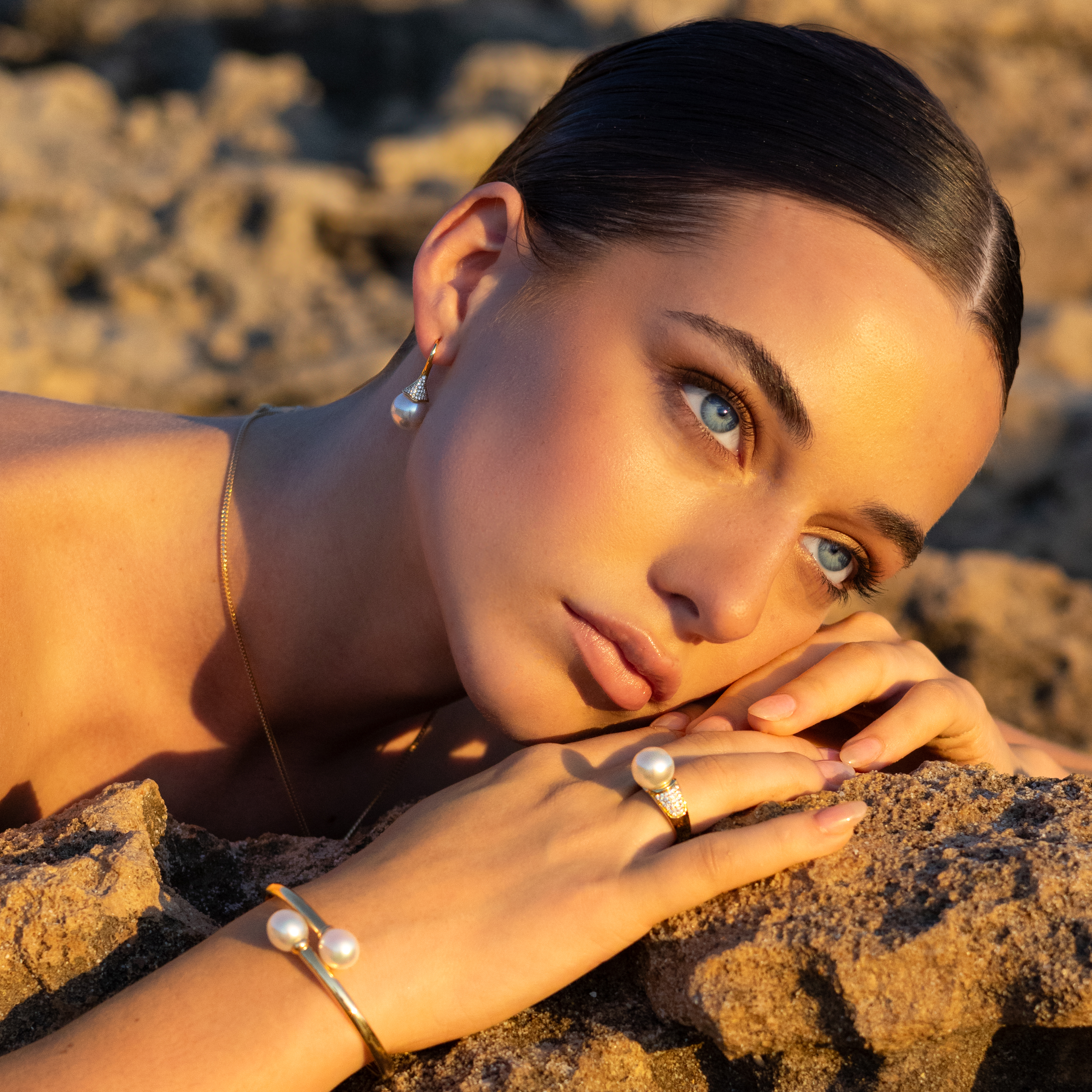 Woman lying on rocks with yellow gold jewelry on, sunlit outdoors